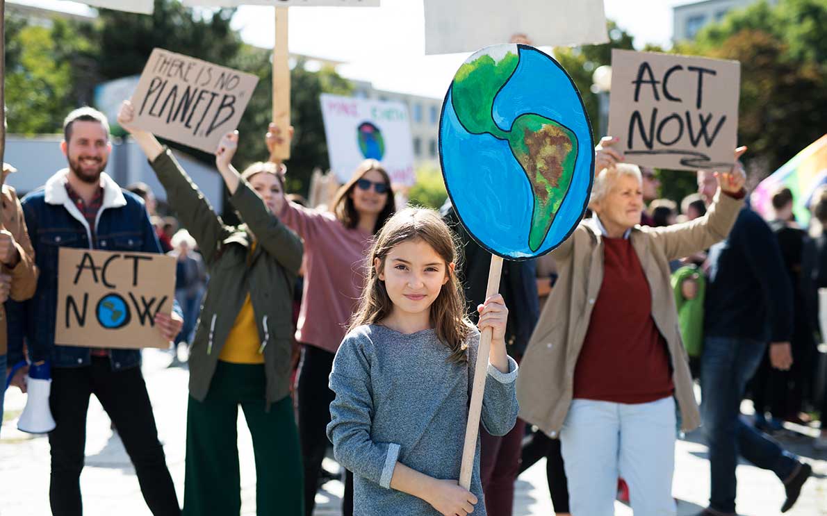 Young girl holding up cardboard Earth sign at environmental activism event