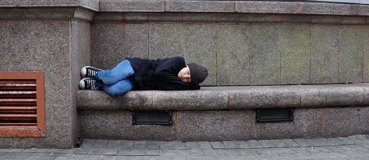 young homeless boy sleeping on a concrete bench