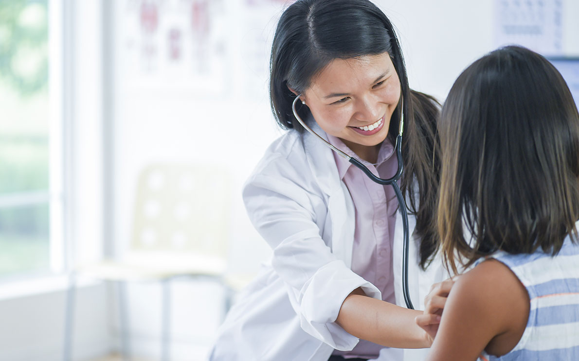 Smiling woman doctor checking young patient with stethoscope